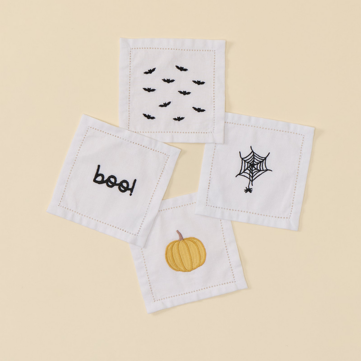 Four white cocktail napkins with Halloween embroidery: bats, pumpkin, boo, and spiderweb.