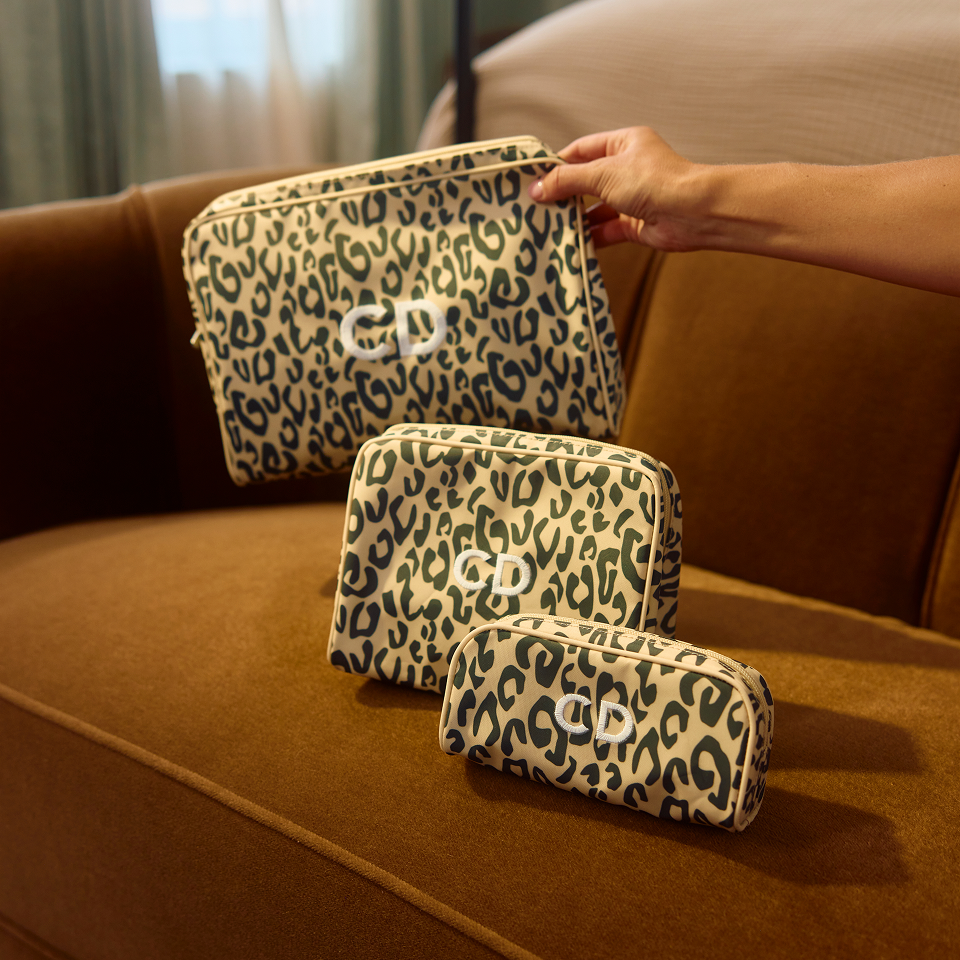 Three leopard-print cosmetic pouches in different sizes set on a brown leather sofa.